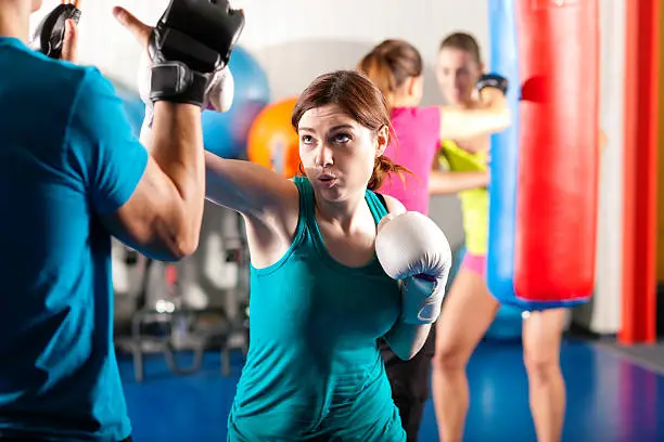Woman Boxer hitting the sandbag her trainer is assisting - Your Savvy Purse