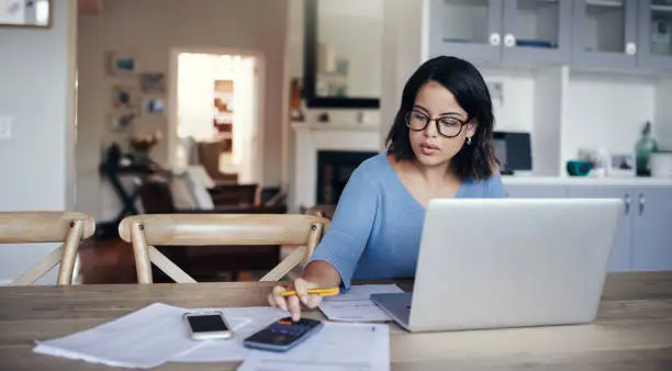 Shot of a young woman using a laptop and calculator while working from home - Your Savvy Purse