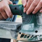 A person sanding a wooden table as part of a DIY furniture makeover