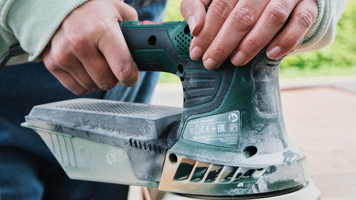 A person sanding a wooden table as part of a DIY furniture makeover