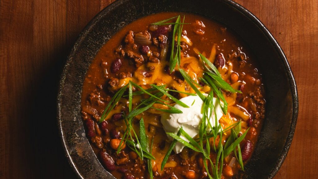A bowl of chili with kidney beans, melted cheese, sour cream and green onions