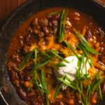 A bowl of chili with kidney beans, melted cheese, sour cream and green onions